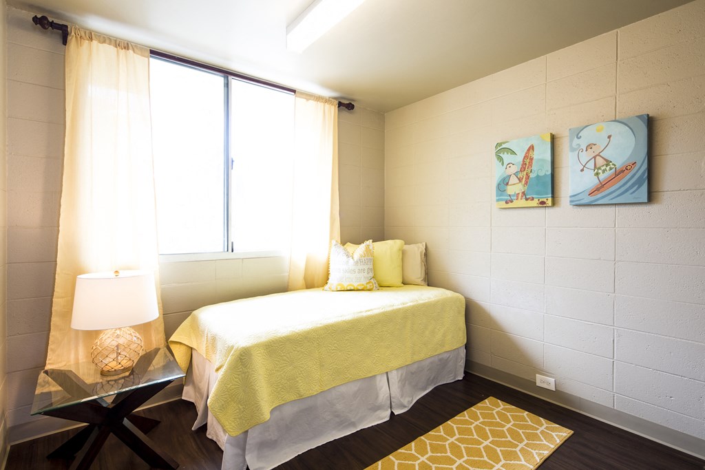 A bedroom with a bed, a table with a lamp, and two paintings on the wall.