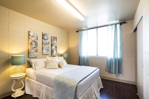 A bedroom with a bed, a nightstand with a lamp, and a window with curtains.