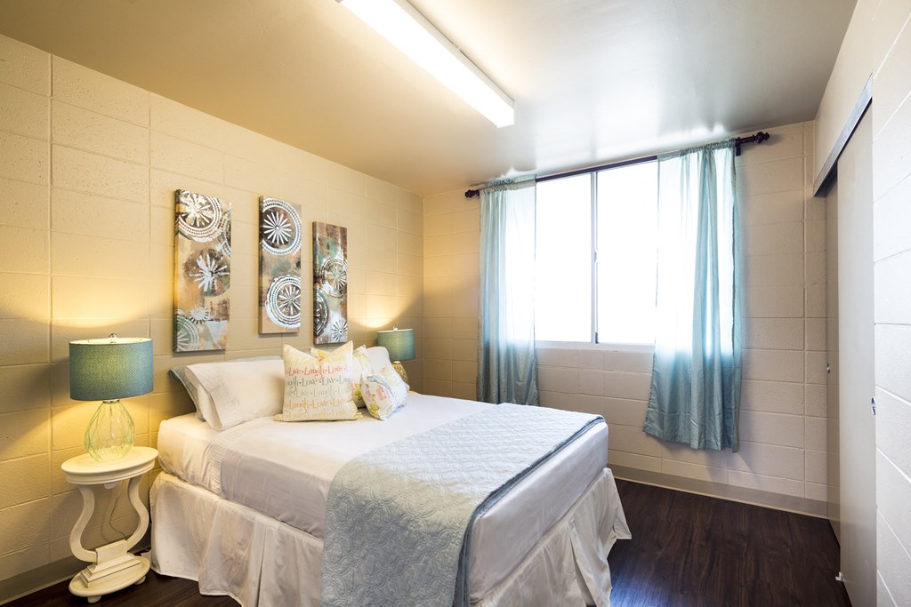 A bedroom with a bed, a nightstand with a lamp, and a window with curtains.