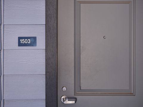 A grey door with a silver handle and a number plate on the wall.
