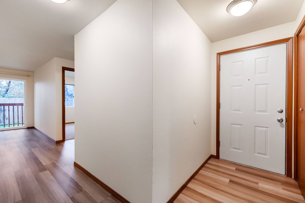 A white door is on the right side of a hallway with wood floors.