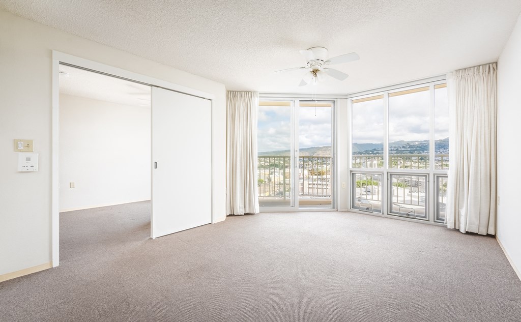 an empty living room with a ceiling fan and large windows