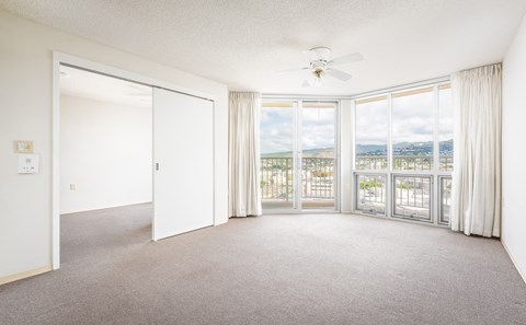 A spacious room with a ceiling fan and sliding glass doors leading to a balcony.