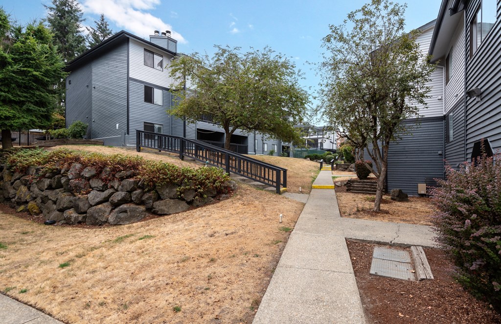 A grey house with a stone wall and a sidewalk.
