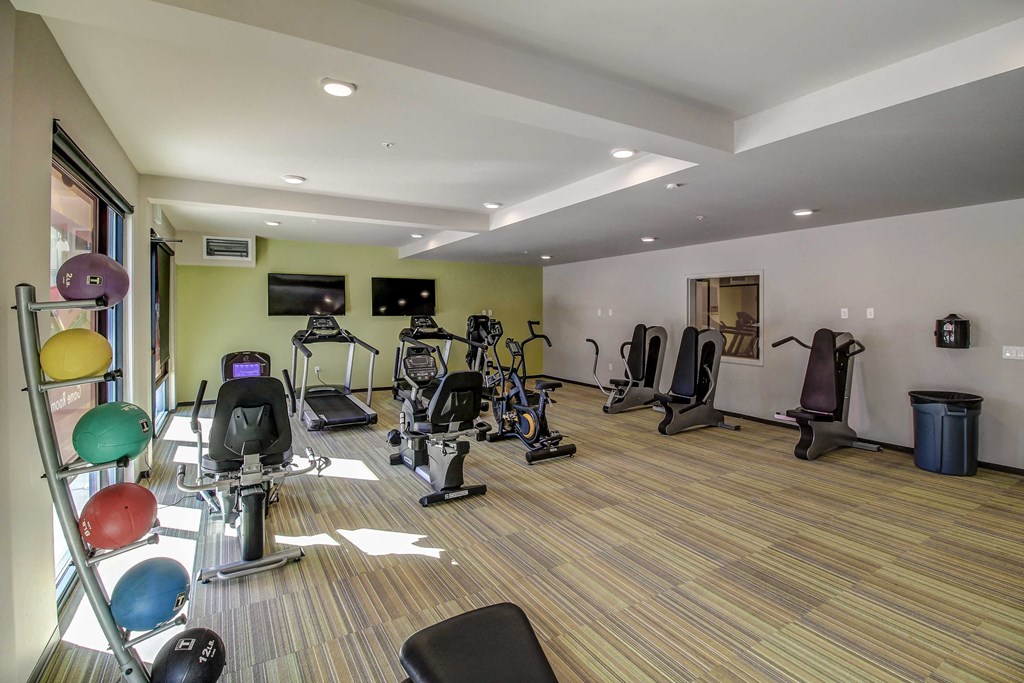 a gym with cardio equipment and weights on a wooden floor