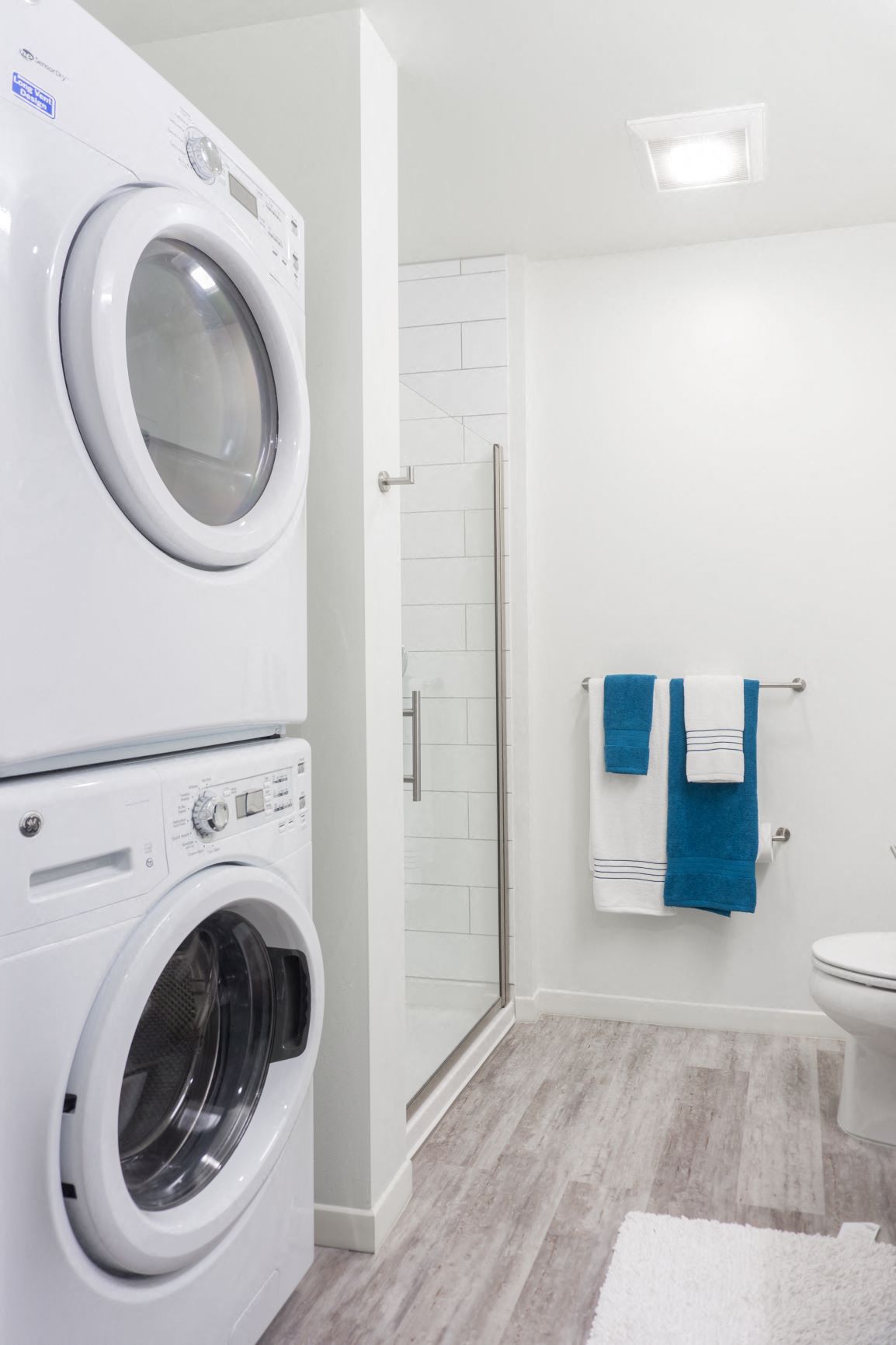 a white washer and dryer in a bathroom with a shower and a toilet