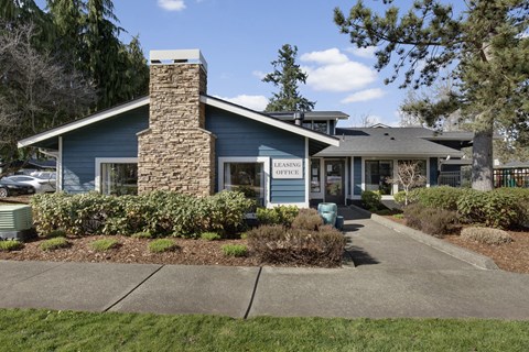 A blue building with a stone chimney and a sign that says "LEASING OFFICE" is surrounded by greenery.