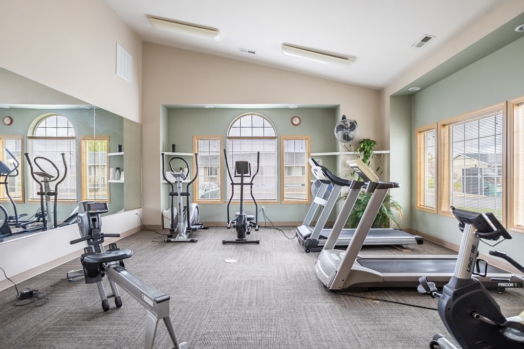 a gym with cardio machines and weights on the floor and windows