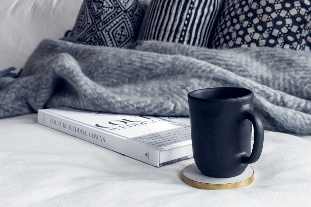 a blue coffee mug sitting next to a book on a bed