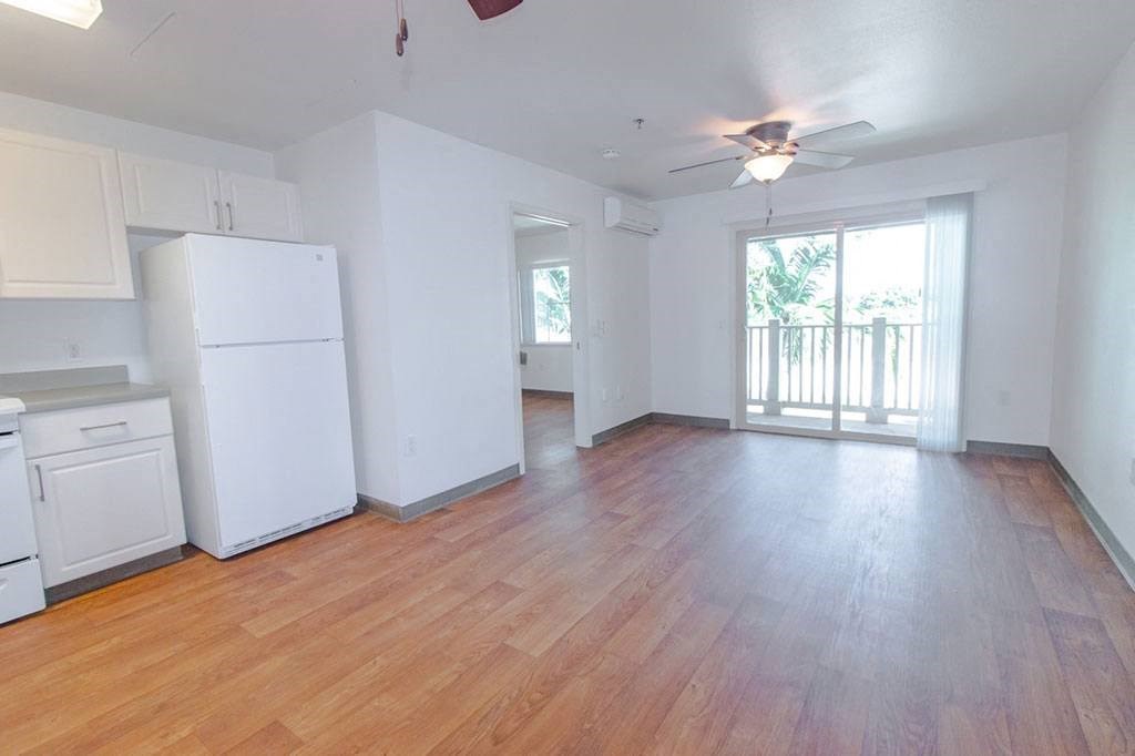an empty living room with a refrigerator and a ceiling fan