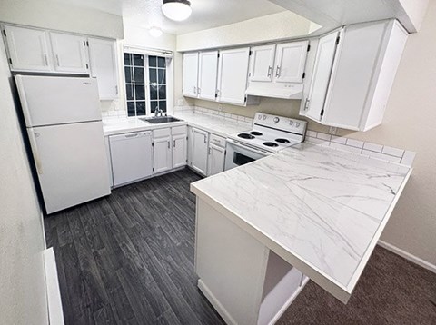 A kitchen with white cabinets and a marble counter.