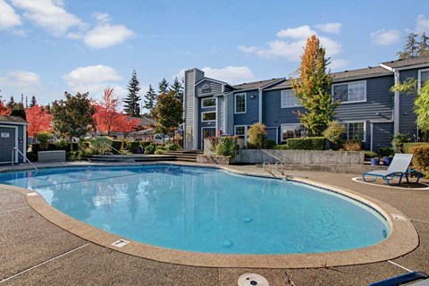 A swimming pool in front of a building with trees in the background.