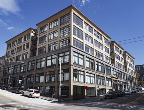 A large building with many windows is situated on a street with cars parked on the side.