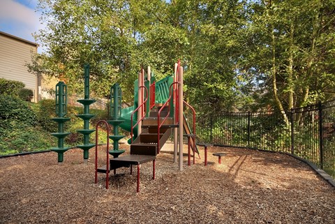 A playground with a red slide and green climbing frame.