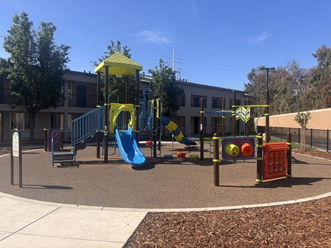 A playground with a yellow and blue slide, a red and yellow structure, and a green and yellow swing set.