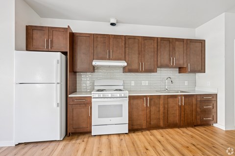 A white refrigerator stands next to a white stove in a kitchen with wooden cabinets.