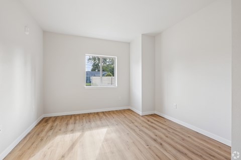 A room with wooden flooring and a window showing a view of trees and a building outside.