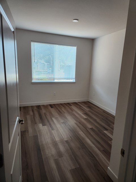 A room with a wooden floor and a window with blinds.