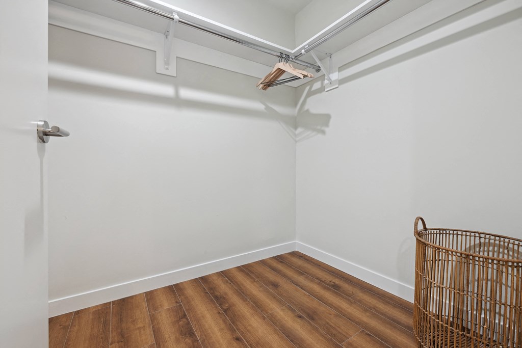 a room with white walls and wooden floors and a wire basket on the wall
