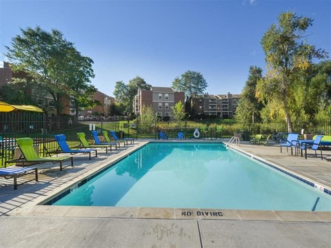 A swimming pool surrounded by chairs and trees with apartment buildings in the background.
