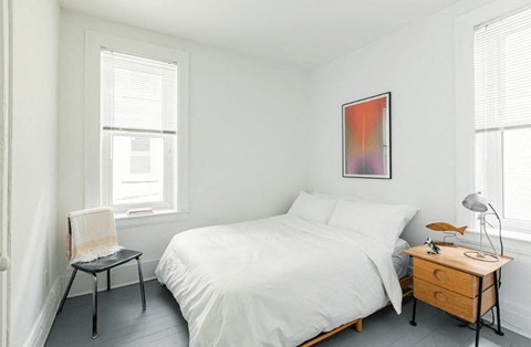 a bedroom with a bed and a dresser and two windows