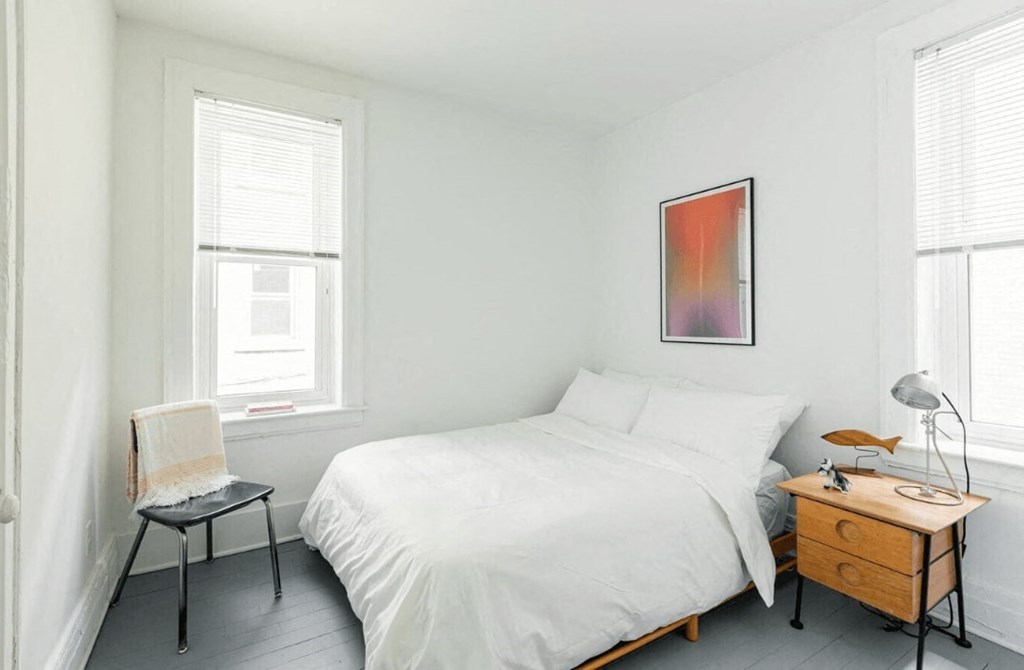 a bedroom with a bed and a dresser and two windows