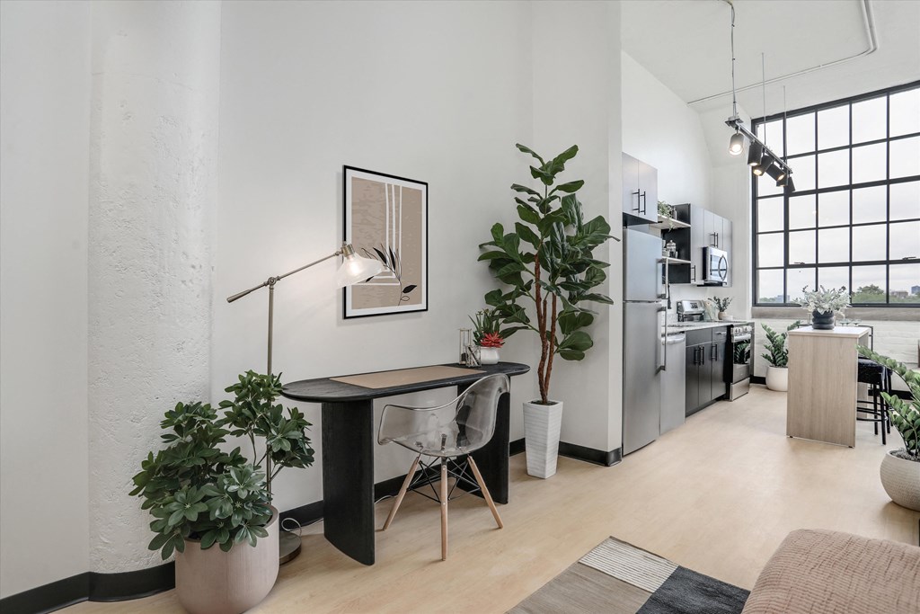 a living room with a desk and a kitchen with plants