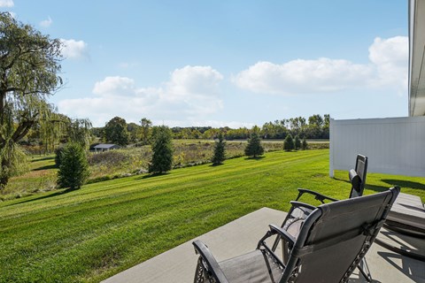 Two chairs are on a patio overlooking a green field.