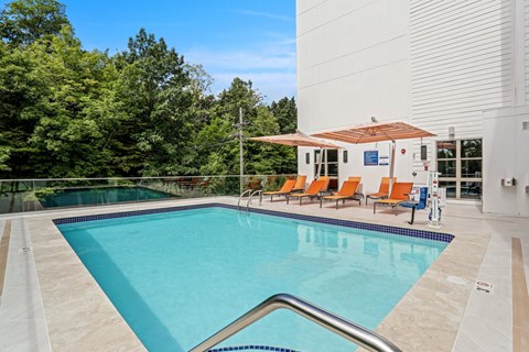 a swimming pool with orange chairs and a building in the background