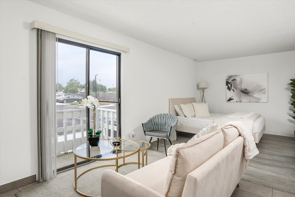 a living room with white furniture and a sliding glass door to a balcony