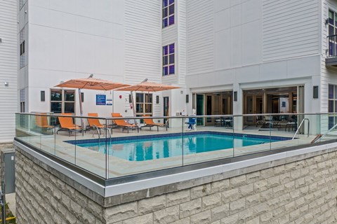 a swimming pool in front of a white building with a glass railing around it
