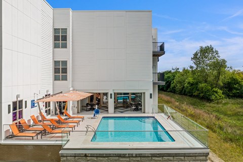 a swimming pool in front of a white building with orange chairs