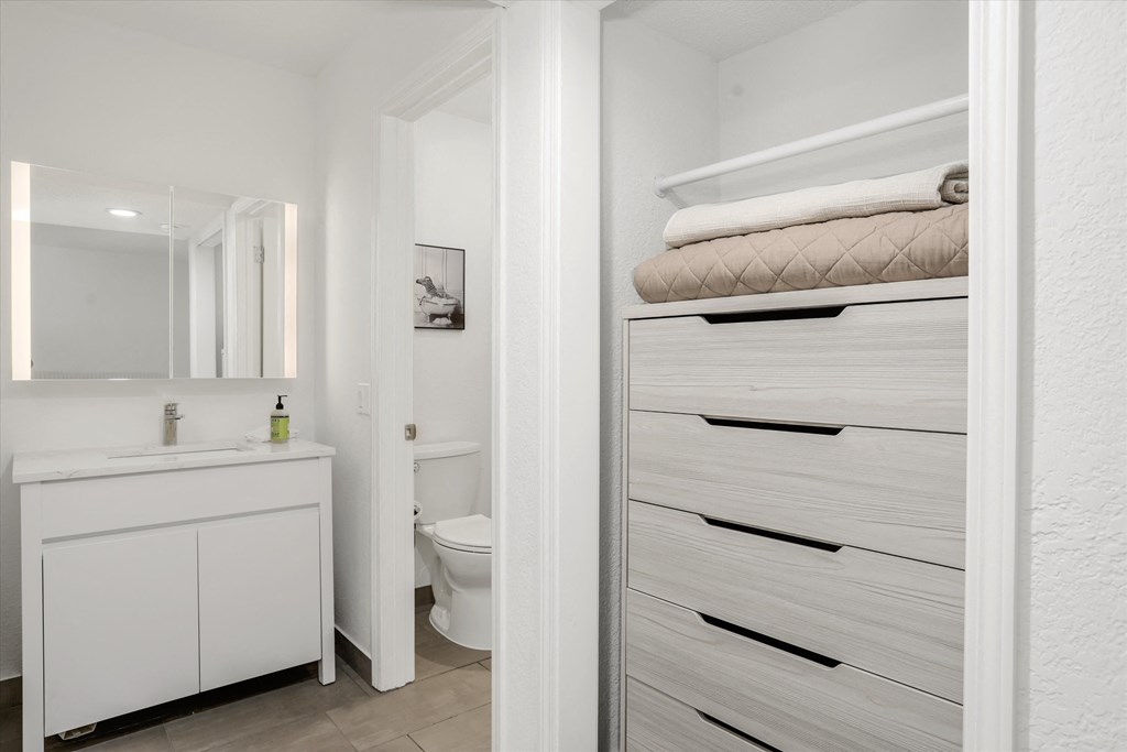 a bathroom with white cabinets and a white toilet and a closet with white towels