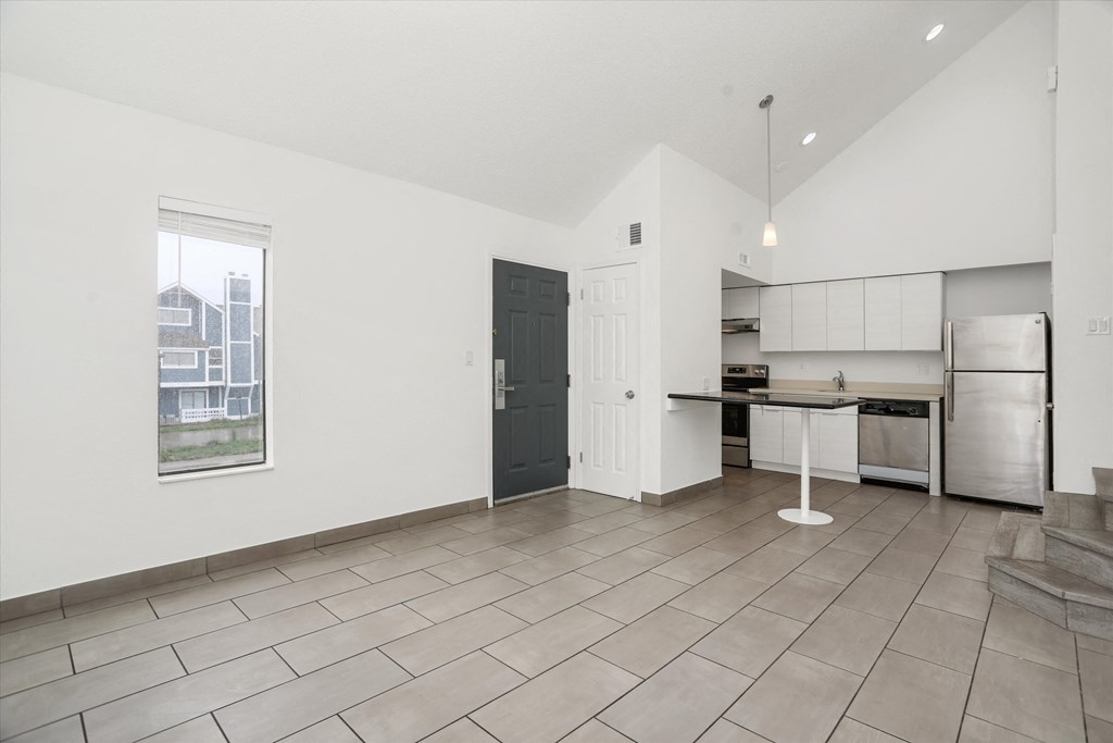 the living room and kitchen of an apartment with white walls and tiled flooring