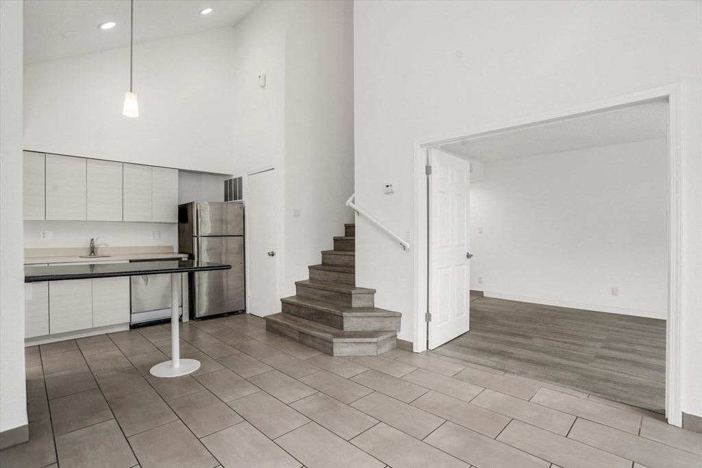 an empty living room with a staircase and a kitchen