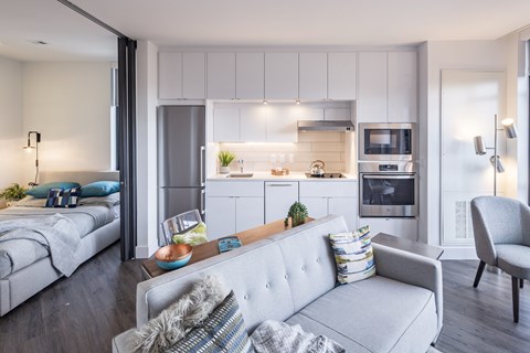 A modern living room with a grey couch and a kitchen area in the background.