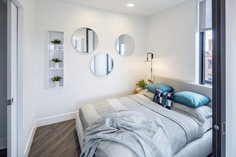 A bedroom with a bed, a nightstand, and three mirrors on the wall.