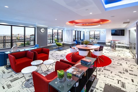 a lounge area with red chairs and tables and a large window