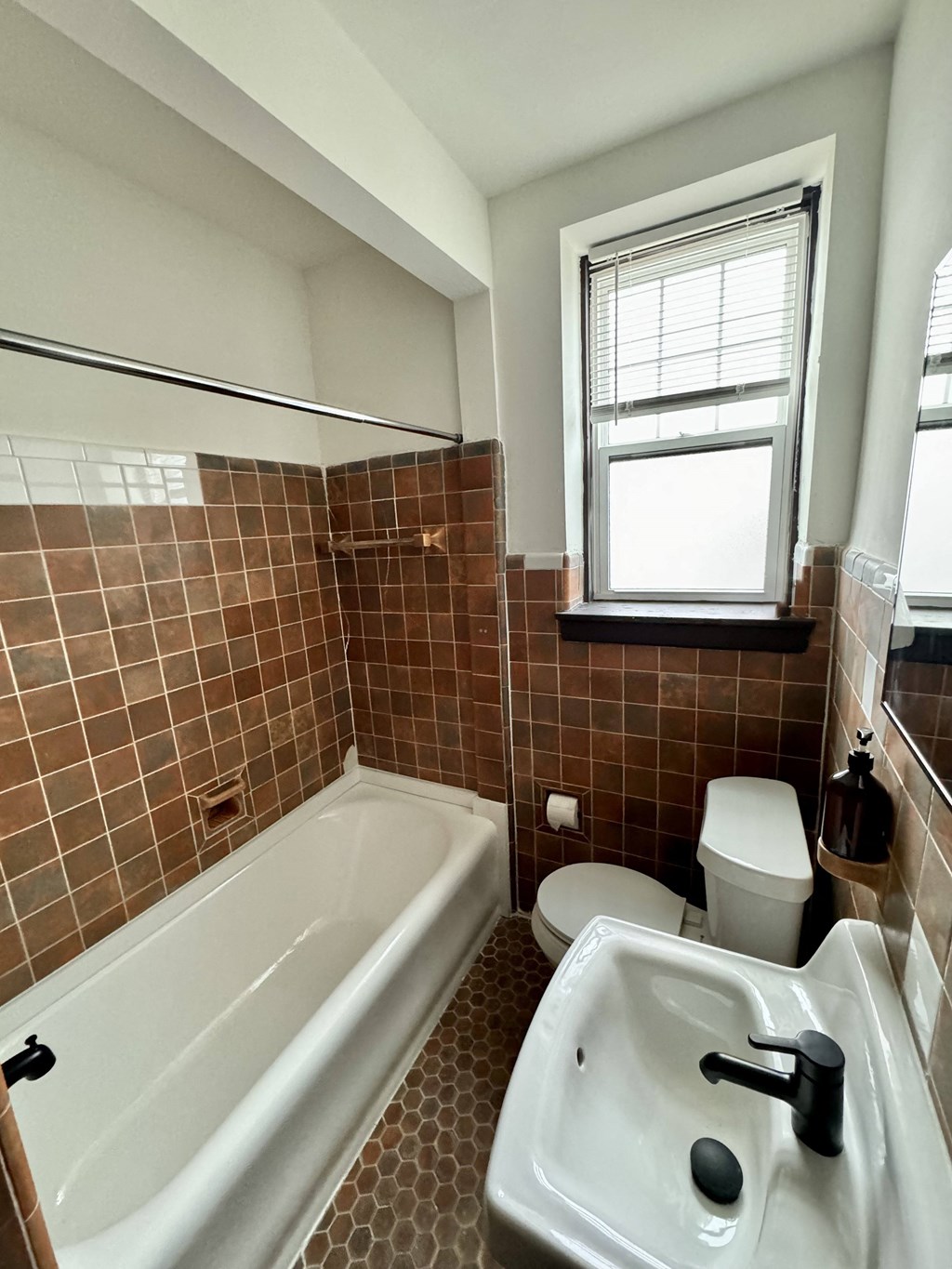 A bathroom with brown tiles and a white tub.