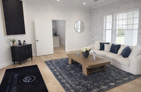 A living room with a white couch, a wooden coffee table, and a black rug with the text "WELINE" on it.