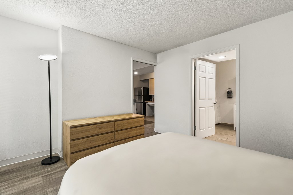 A white bedroom with a bed, dresser, and lamp.
