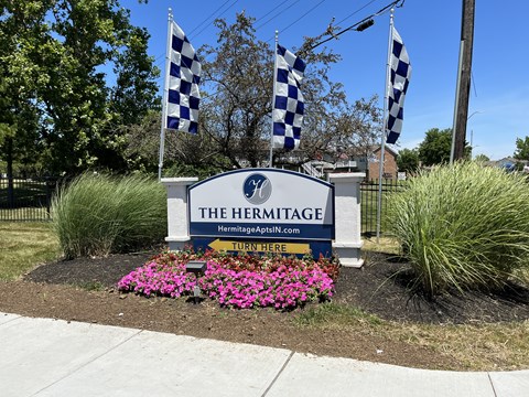 A sign for The Hermitage with flags and flowers in front.