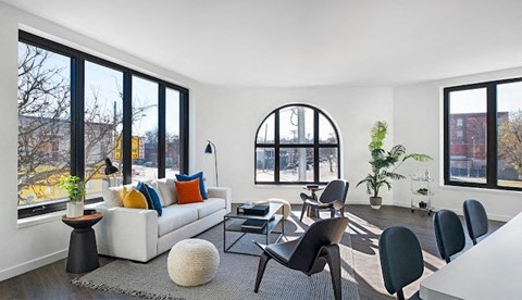 A living room with a white couch, a round mirror, and a large window.