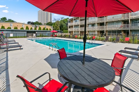 A table with chairs and an umbrella is in front of a pool.