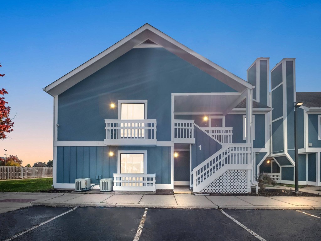 the front of a blue house with a porch and a parking lot