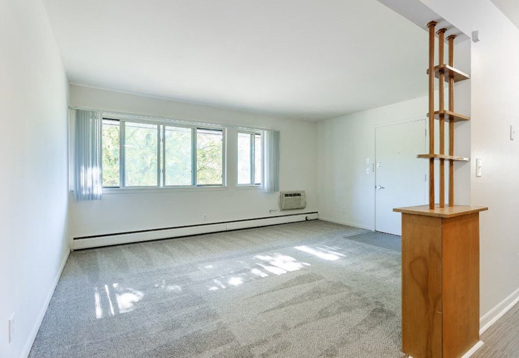 an empty living room with a large window and a wooden piece of furniture