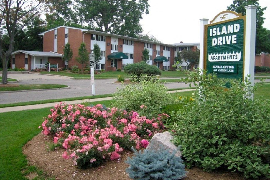 a sign for island drive apartments in front of a flower garden