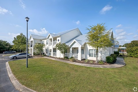 A white house with a grey roof and a grey car parked in front.