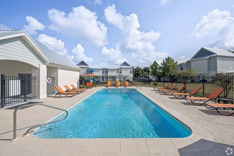 A large swimming pool surrounded by lounge chairs and buildings.
