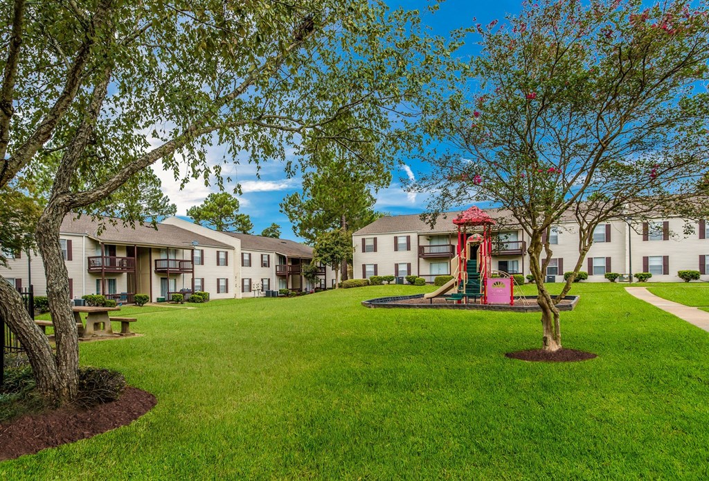 a park with green grass and trees in front of apartment buildings